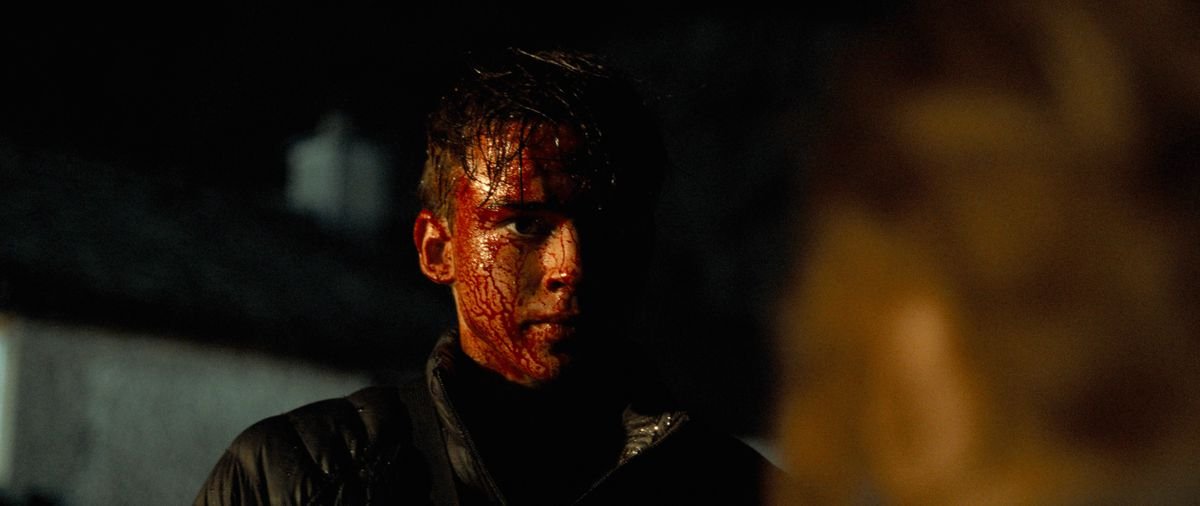 Joseph (Jaeden Martell) stands outdoors at night, soaked in blood and looking grim, in Arcadian