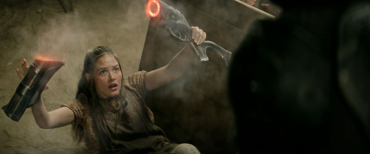 Charlotte Maggi as Sam falls backward on the floor holding a sliced-in-half gun in Rebel Moon — Part Two: The Scargiver